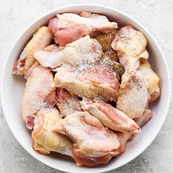A bowl of raw chicken wings seasoned with spices.