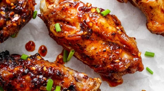 Glazed chicken wings on parchment paper garnished with sesame seeds and chopped green onions.