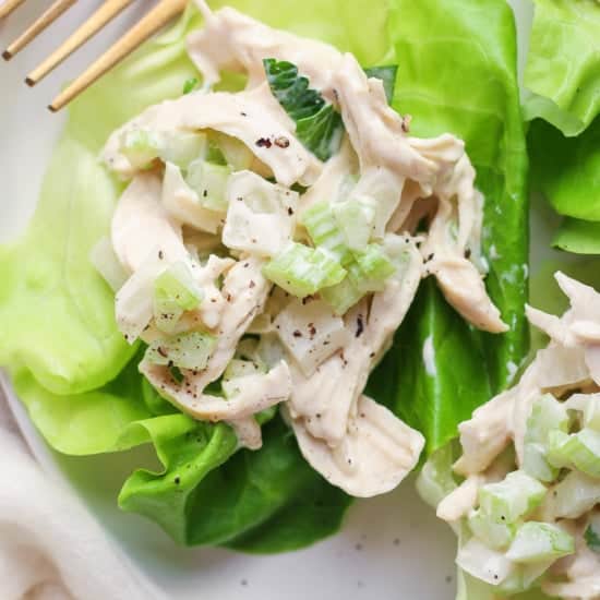 A chicken salad with creamy dressing served on a fresh lettuce leaf with a pair of gold forks on the side.