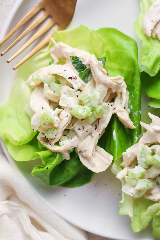 A chicken salad with creamy dressing served on a fresh lettuce leaf with a pair of gold forks on the side.