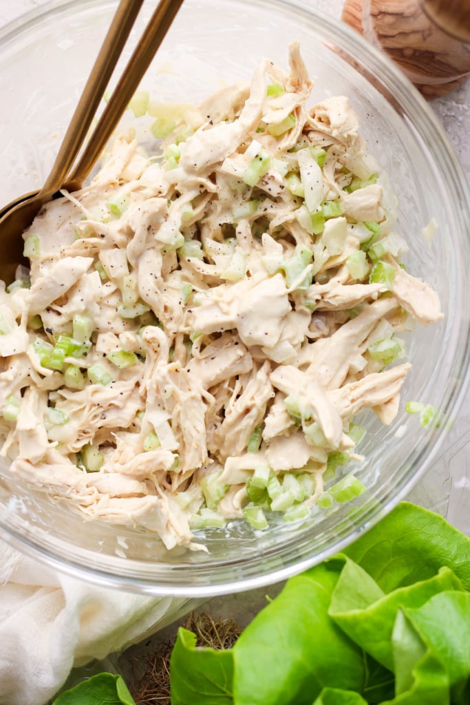 Shredded chicken mixed with chopped green onions and seasoning in a glass bowl.
