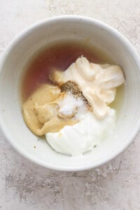 A bowl containing ingredients such as a liquid (possibly vanilla extract or a similar flavoring), spices, and creamy substances like mayonnaise, sour cream, or yogurt, with a sprinkling of fine.