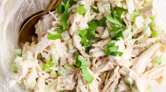 A bowl of shredded chicken salad garnished with chopped green onions and herbs.