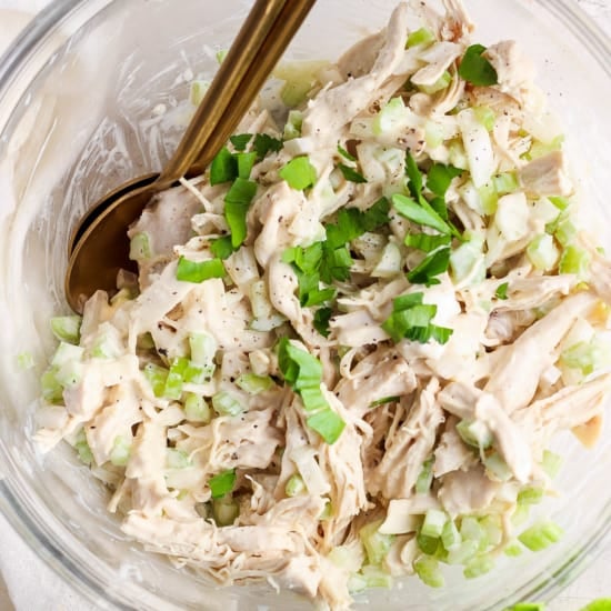 A bowl of shredded chicken salad garnished with chopped green onions and herbs.