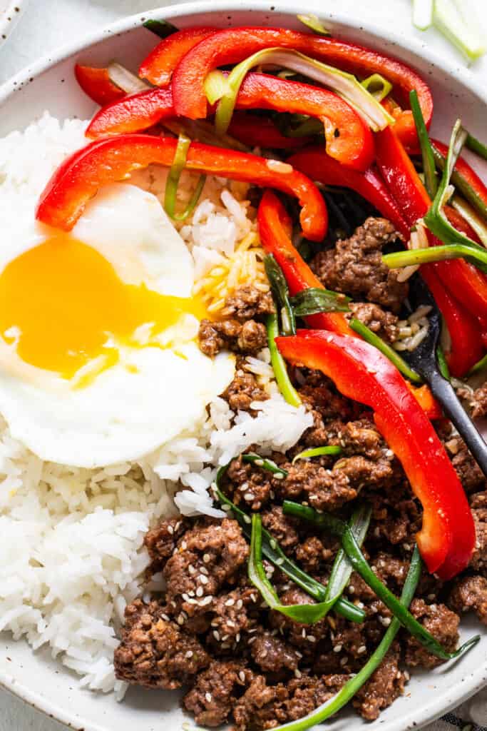 Bibimbap with Korean ground beef, vegetables, and a sunny-side-up egg in a bowl.