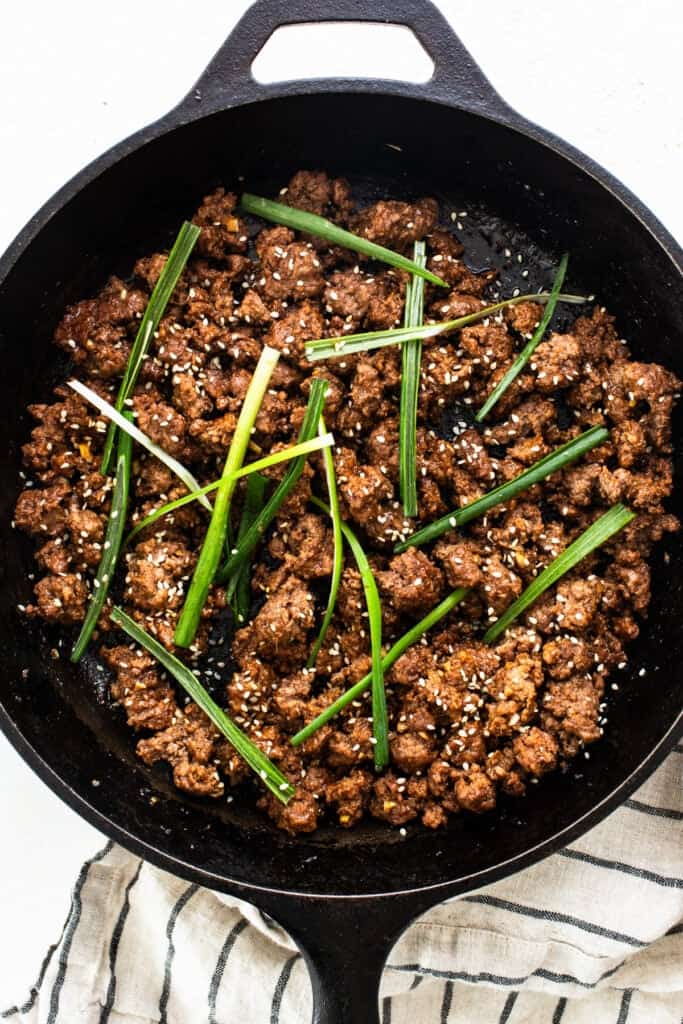 Cooked Korean ground beef garnished with green onions and sesame seeds in a cast iron skillet.
