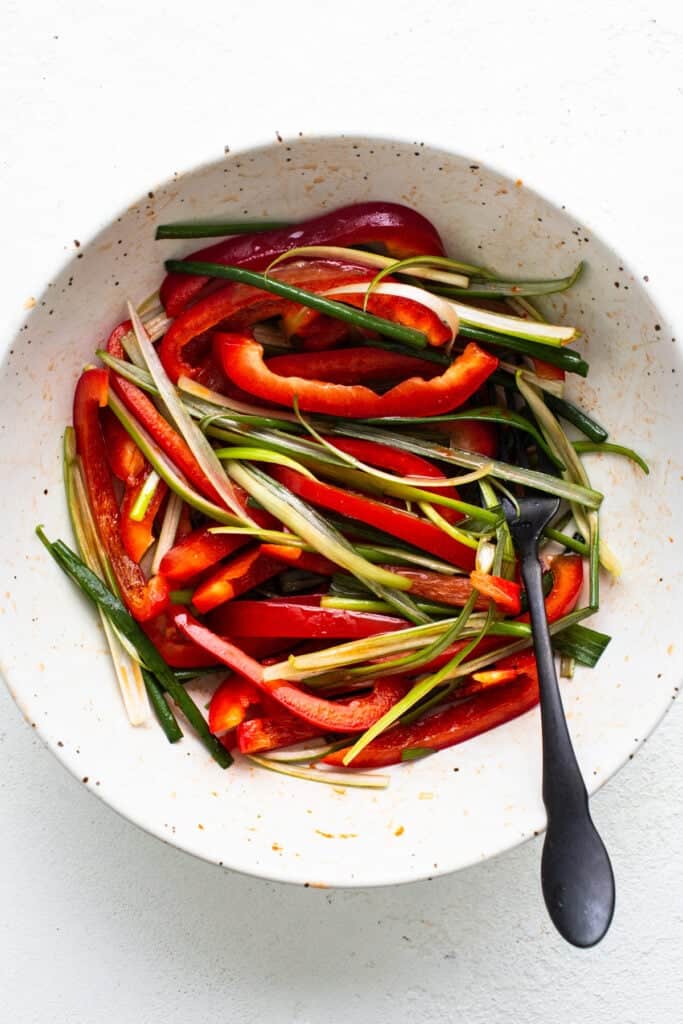 A bowl of sliced red bell peppers and green beans ready for cooking with Korean ground beef, accompanied by a spoon.