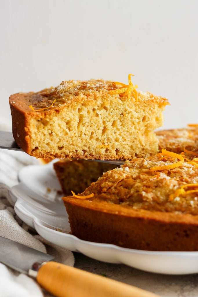 A freshly baked orange cake with a slice partially lifted out, showcasing its moist crumb and topped with orange zest.