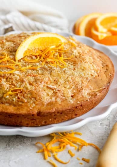 A freshly baked orange cake garnished with orange zest on a white plate.