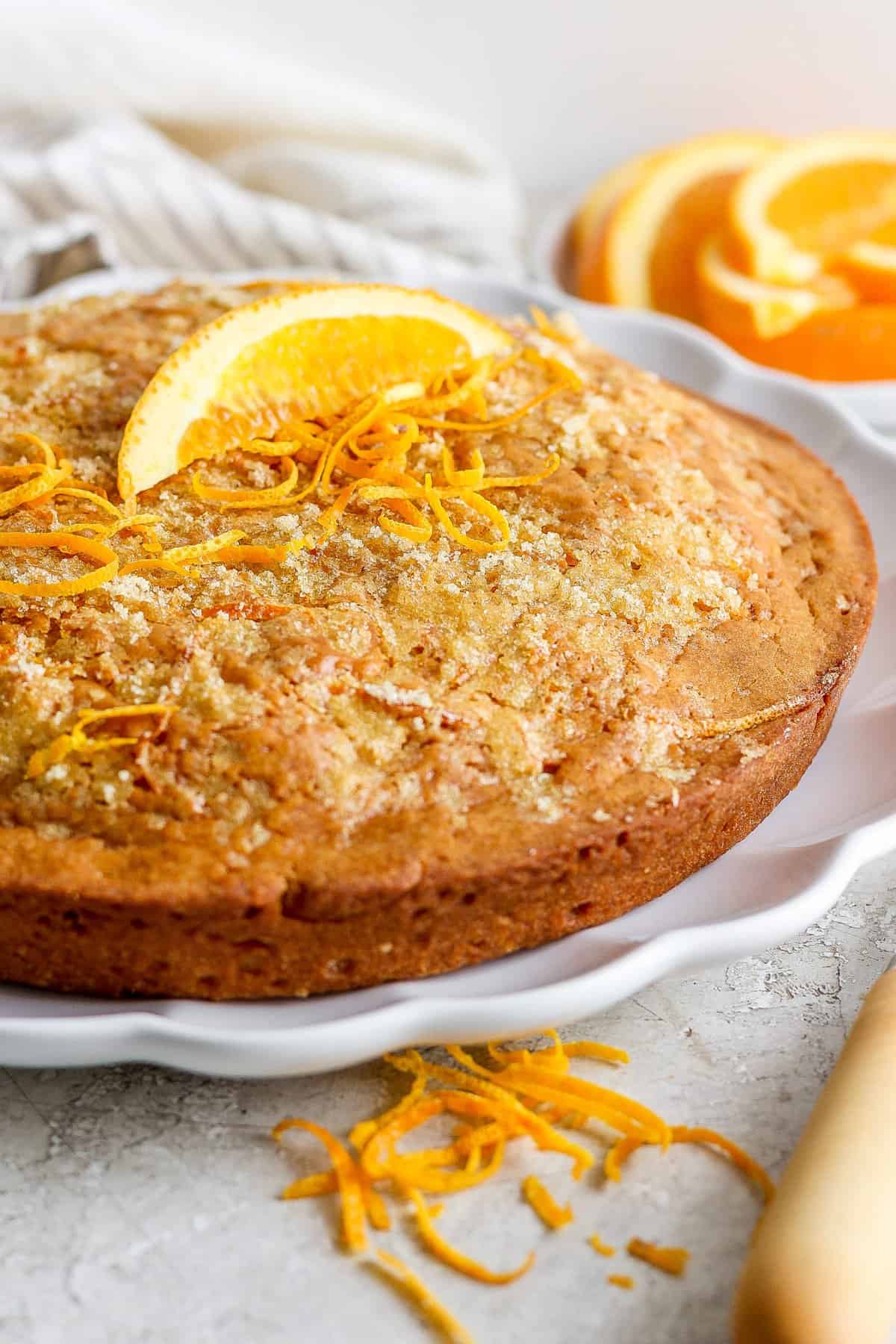 A freshly baked orange cake garnished with orange zest on a white plate.