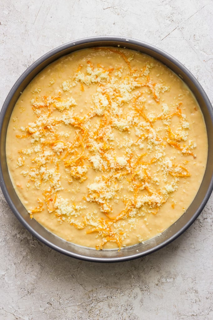Unbaked cheesecake with crumbled topping in a round pan.