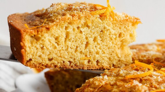 A sliced citrus-flavored pound cake with orange zest garnish on a white plate.