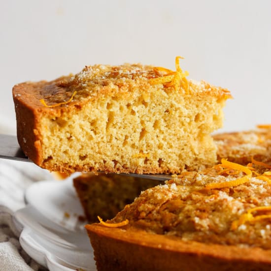 A sliced citrus-flavored pound cake with orange zest garnish on a white plate.