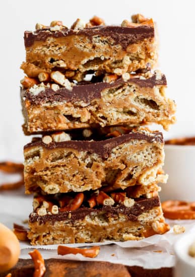 A stack of three layered peanut butter bars with a chocolate topping and crushed nuts on parchment paper.