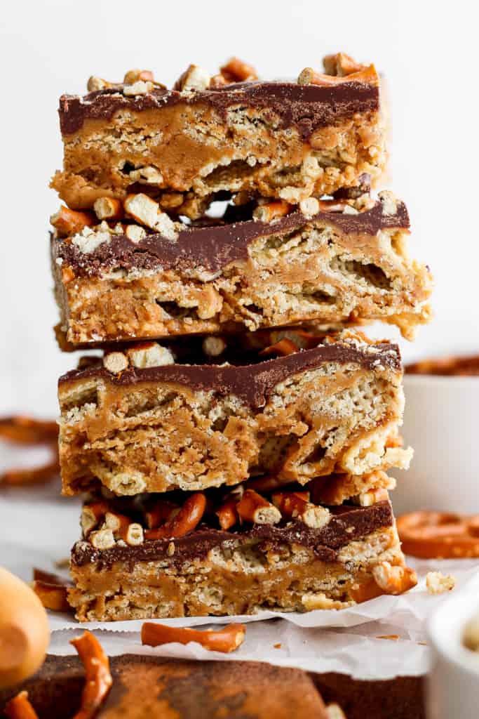 A stack of three layered peanut ،er bars with a c،colate topping and crushed nuts on parchment paper.