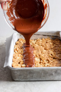 Chocolate sauce being poured onto a tray of baked dessert bars.