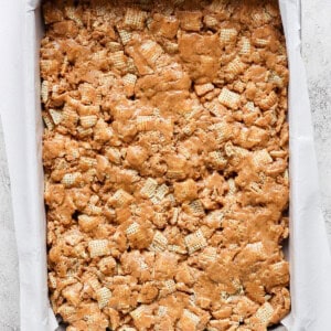A baking tray filled with a peanut butter rice krispie treats mixture, lined with parchment paper on a light textured surface.