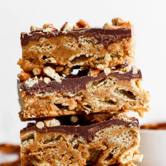 Stack of three peanut butter rice krispie treats topped with a layer of chocolate and sprinkled with chopped peanuts.