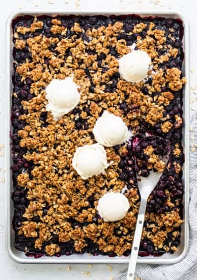 Freshly baked blueberry crumble with scoops of vanilla ice cream on top.