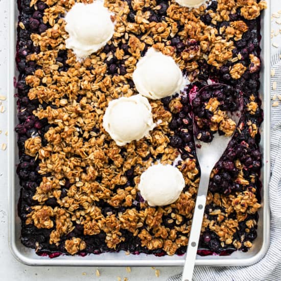 Homemade blueberry crumble with scoops of vanilla ice cream on top.