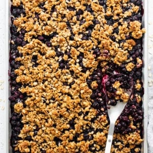 A baked blueberry oatmeal crumble in a rectangular pan with a serving spoon.