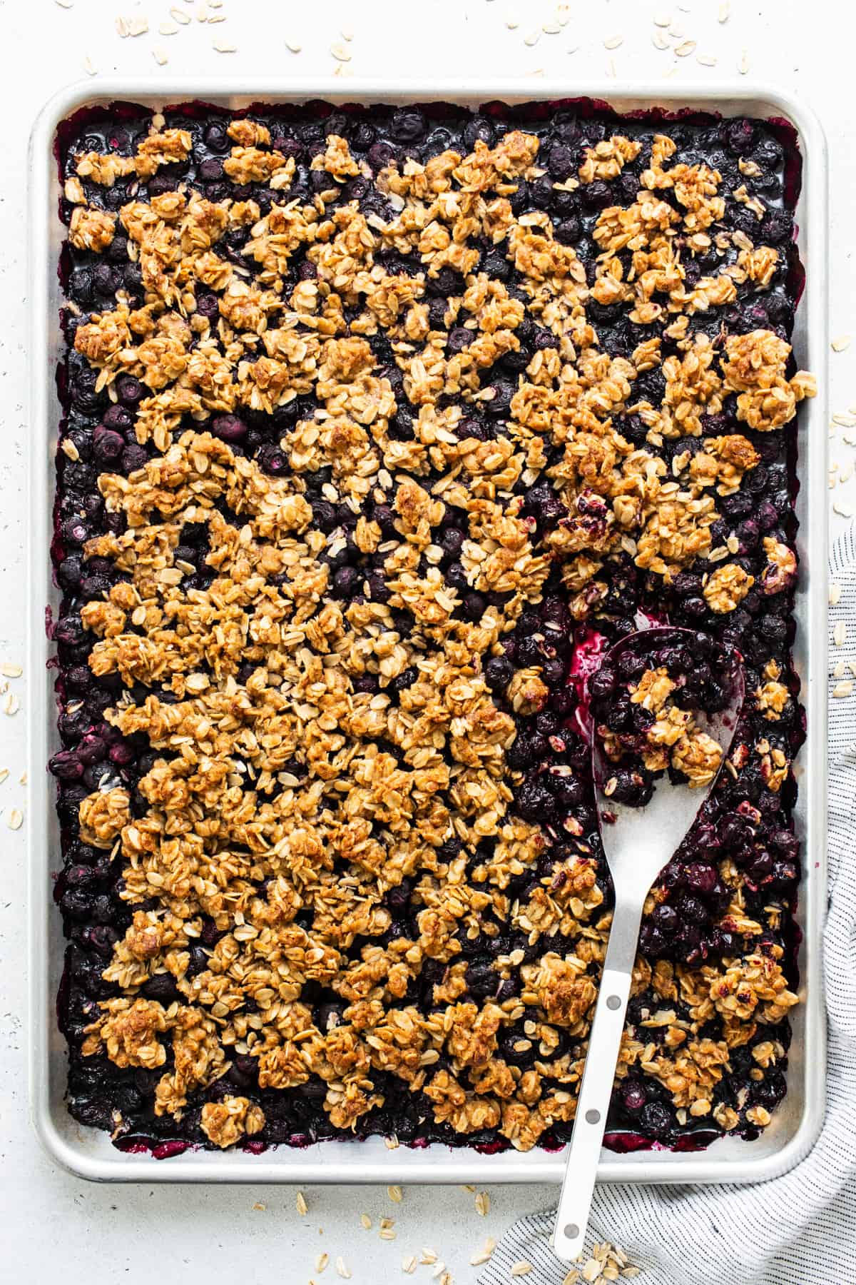 A baked blueberry oatmeal crumble in a rectangular pan with a serving spoon.
