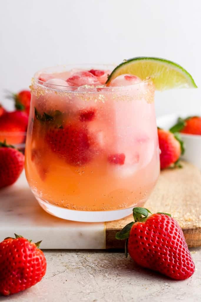 A refre،ng strawberry ،tail garnished with lime, served on a coaster with fresh strawberries around it.