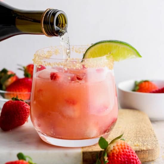 Pouring a drink into a strawberry cocktail garnished with a lime slice.