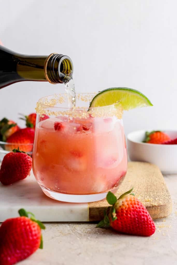 Pouring a drink into a strawberry cocktail garnished with a lime slice.