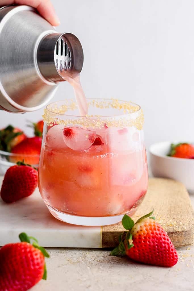 Pouring a beverage into a glass rimmed with sugar, accompanied by fresh strawberries.