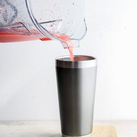 Pouring a red smoothie into a metal tumbler.