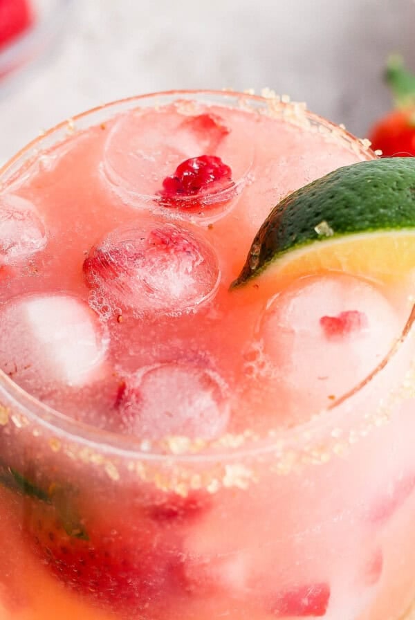 A refreshing strawberry cocktail with ice, lime, and a sugared rim.