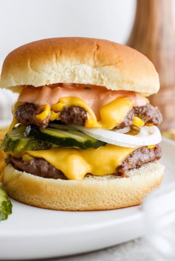 A double cheeseburger with pickles, onions, and sauce on a white plate.