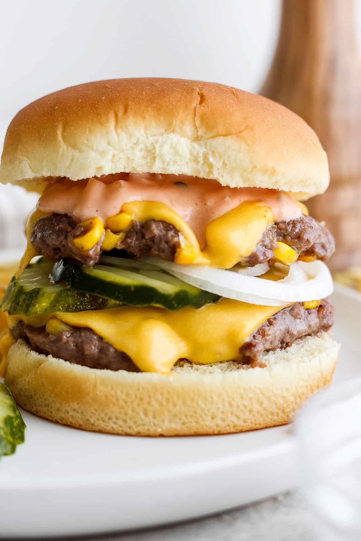 A double cheeseburger with pickles, onions, and sauce on a white plate.