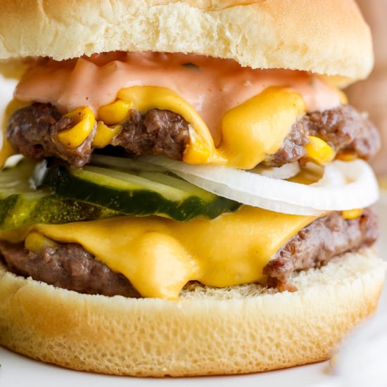 Close-up of a double cheeseburger with melted cheese, pickles, and onions.