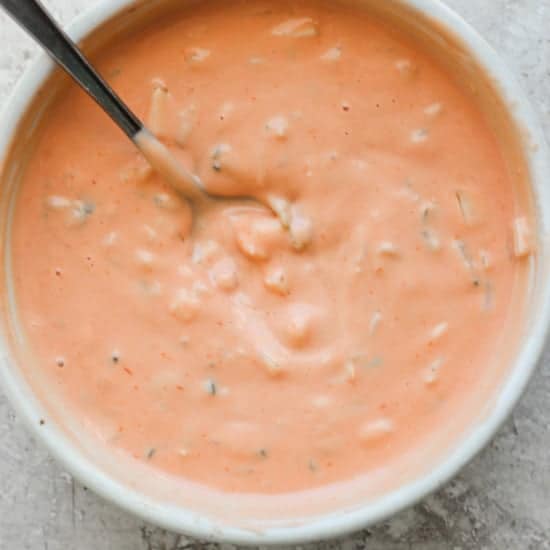 A bowl of creamy tomato soup with herbs, served with a spoon.