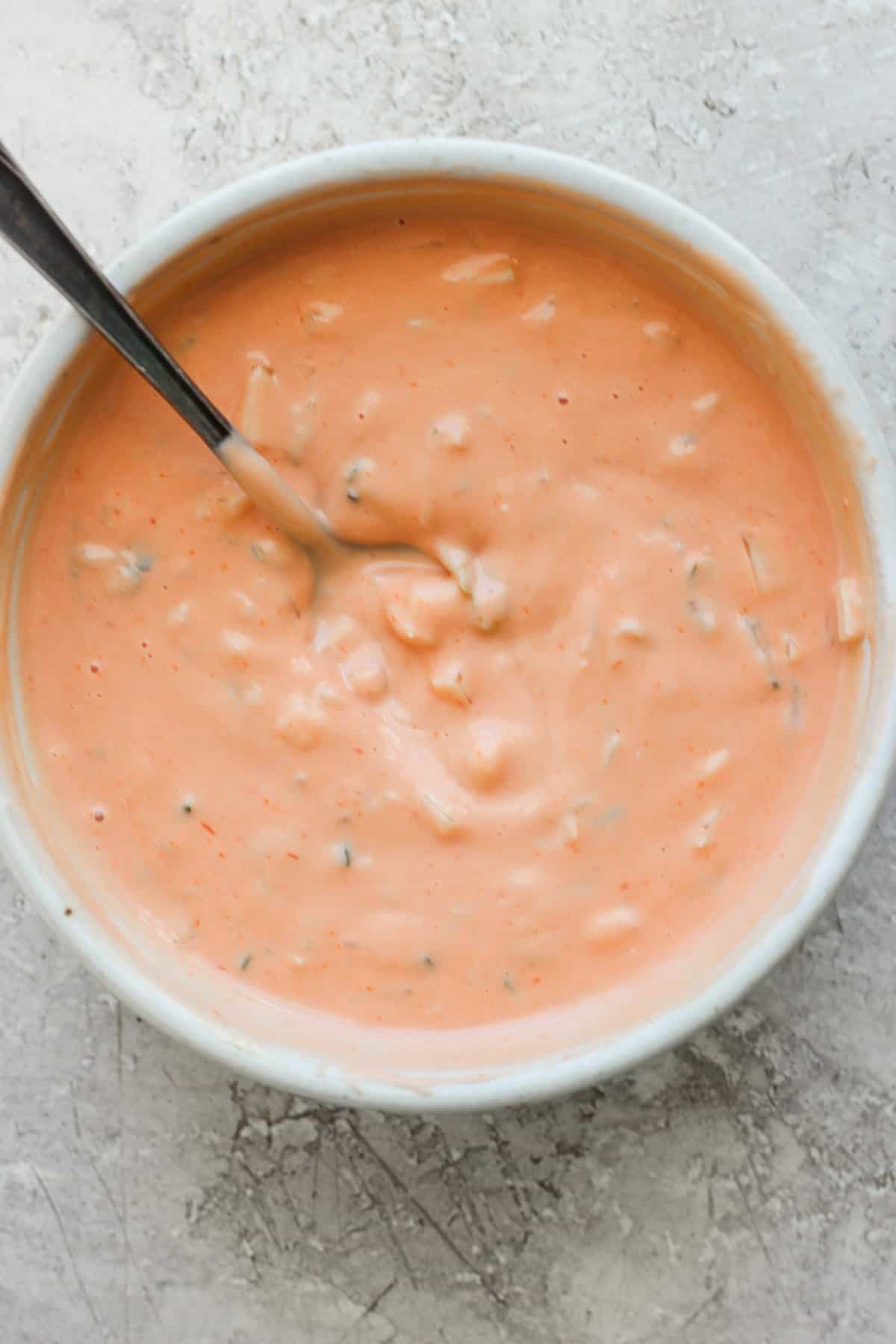A bowl of creamy tomato soup with herbs, served with a spoon.