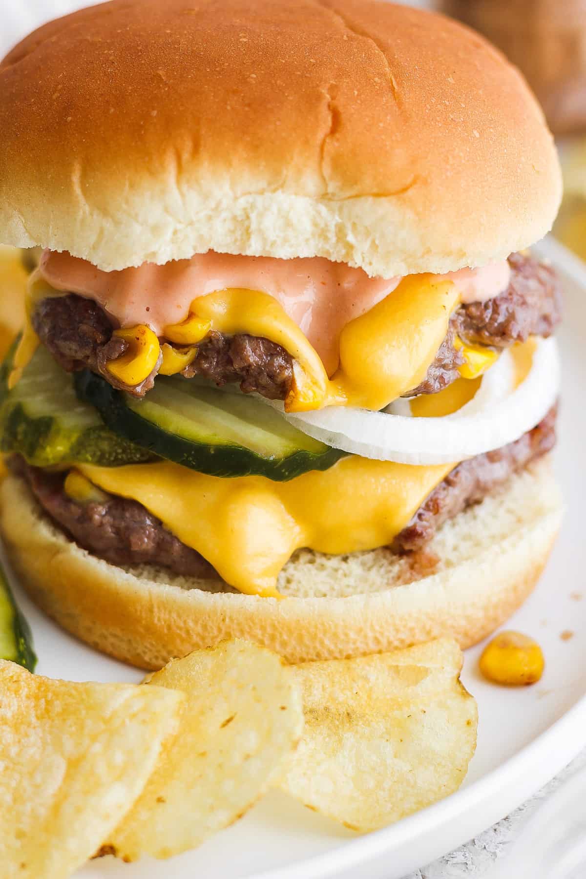Cheeseburger with lettuce, pickles, and sauce served with potato chips.