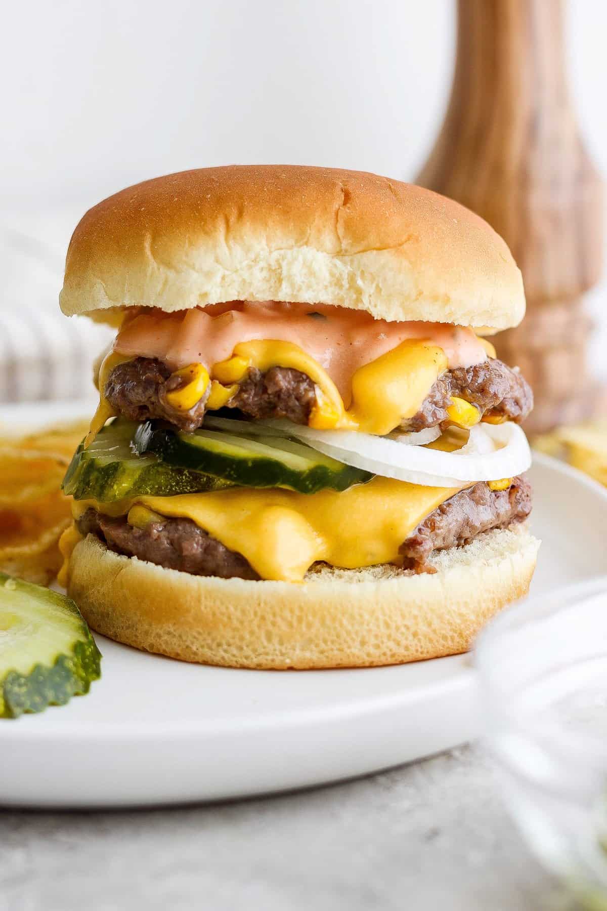 Double cheeseburger with pickles on a white plate.