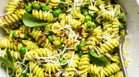 A bowl of pesto pasta garnished with peas, grated cheese, and basil leaves.