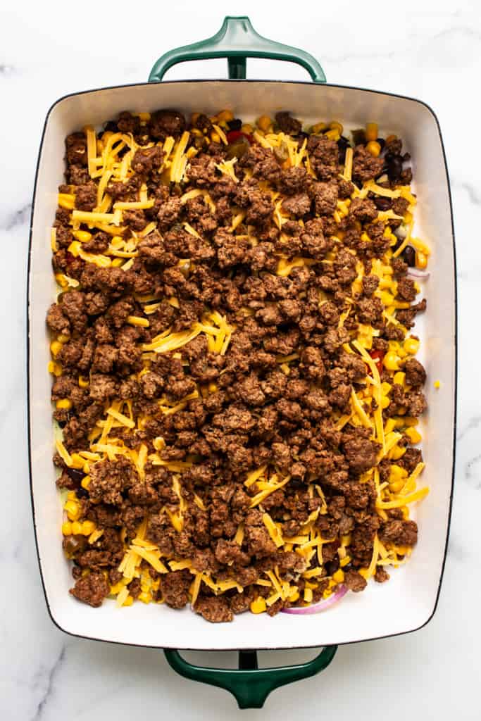 A baking dish with layers of ground beef, corn, and shredded cheese.