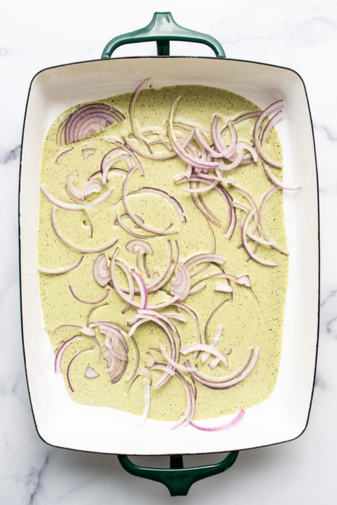 A ceramic dish containing a creamy mixture topped with thinly sliced red onions.