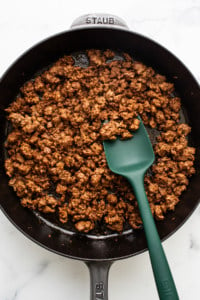 Cooked ground meat in a black cast iron skillet with a green spatula.