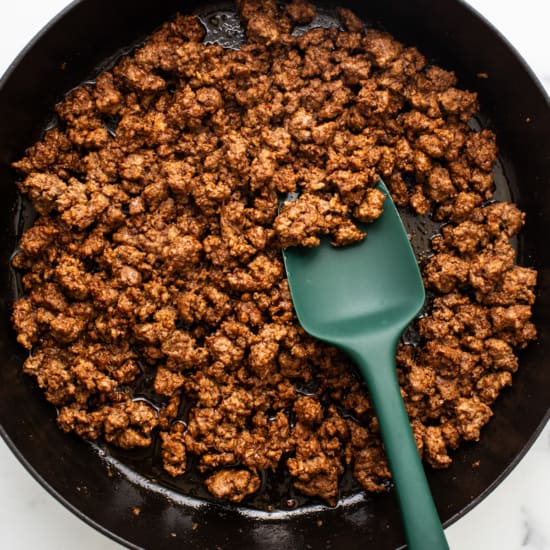 Cooked ground meat in a black cast iron skillet with a green spatula.