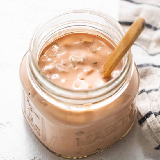 A jar of creamy homemade thousand island dressing with a wooden spoon.