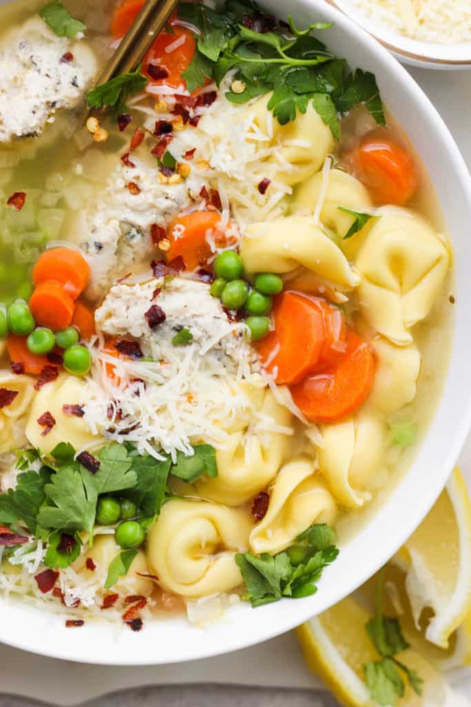 A bowl of chicken noodle soup with vegetables, garnished with parsley and grated cheese.