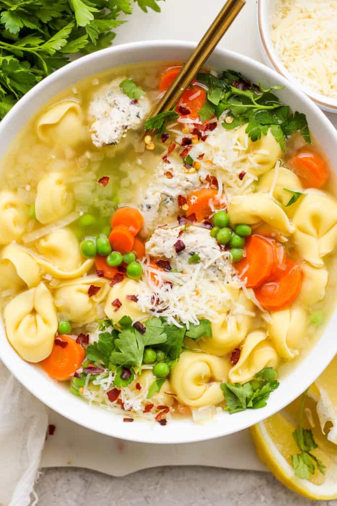A bowl of chicken noodle soup with vegetables, topped with parmesan cheese and fresh herbs.