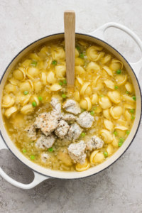 Pot of chicken noodle soup with green peas and a wooden spoon.