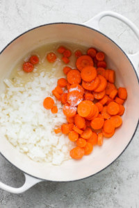 Diced onions and sliced carrots with seasoning in a cooking pot.