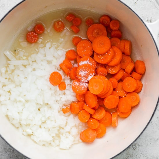 Diced onions and sliced carrots with seasoning in a cooking pot.